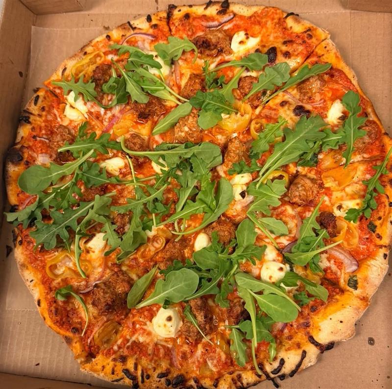 Sausage and banana pepper pizza topped with fresh arugula, top-down